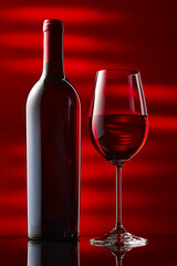 A bottle and a glass of red wine stand on a black mirror table.