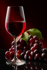 A glass of red wine and grapes on a glossy table.