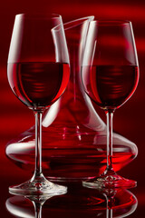 Still life with a decanter and two glasses of red wine on a glossy table.
