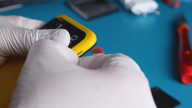 Technician worker pull out SIM tray with SIM cards from yellow smartphone. Hand in white gloves. Subscriber's electronic module used in mobile communications. 5g network or internet concept