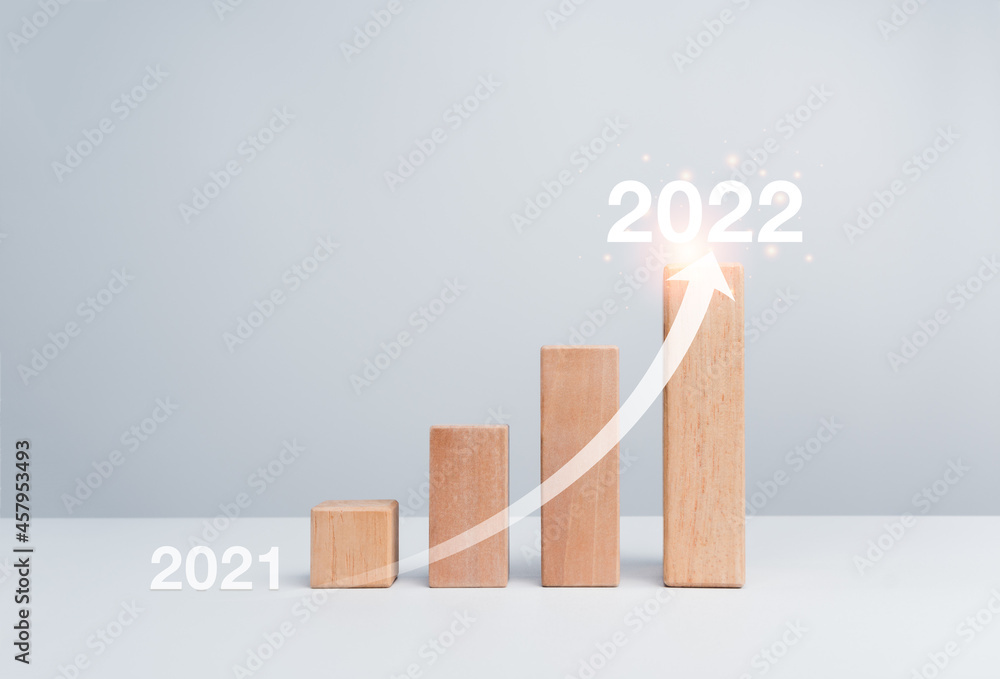 Poster shining rise up arrow on wooden blocks chart steps from the year 2021 to 2022 on white background wi
