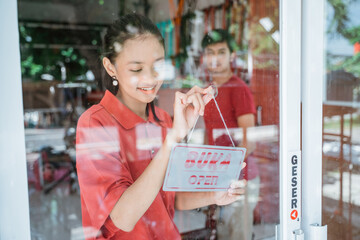 a woman in a red t-shirt prepares to open a shop by posting an open sign on the windshield door