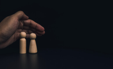 Insurance collateral concept. Hand protecting family wooden figures, male and female, couple on dark background with copy space.