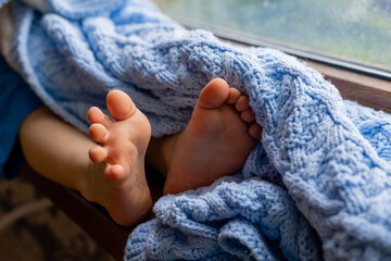closeup of the legs of a sitting child with bare feet covered with a blue knitted blanket....