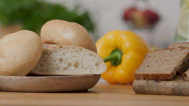 Slide right shot 4k of two types of bread, white bread made of wheat flour and wholemeal rye bread. Slices of bread on wooden plates. Yellow pepper and other vegetables in the background