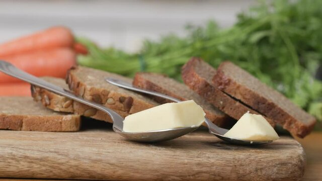 Wooden cutting board with slices of wholemeal bread and two servings of butter. Healthy choice for weight watchers. Slide shot left 4k