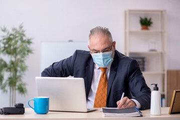 Old male employee working in the office during pandemic