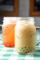 Row of fresh boba bubble tea glasses on wooden table with green plaid tablecloth background.