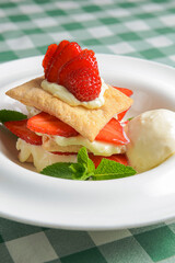 Puff pastries with strawberries and berry sauce on a white plate. Over green plaid background.