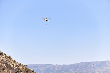 Firefighting helicopter transporting water to extinguish a forest fire. Hazard concept