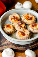 Georgian traditional dish Stuffed mushrooms served in a bowl with a lot of fresh greenery on rustic wooden table.