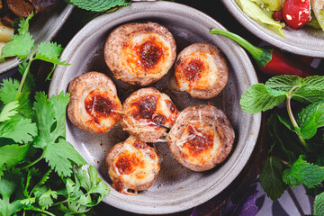 Georgian traditional dish Stuffed mushrooms served in a bowl with a lot of fresh greenery on rustic wooden table.