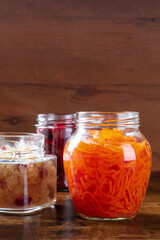 Fototapeta na wymiar Glass jars of pickled carrot, sour cabbage and other fermented foods. Canning vegetables, homemade preserves concept with copy space on a dark rustic wooden background
