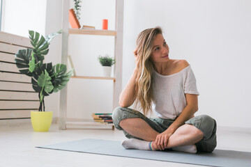 Fototapeta na wymiar Positive girl sitting on fitness mat resting after pilates or yoga practice. Mindfulness and wellbeing concept.