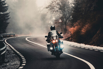 Motorcyclist travels through foggy autumn mountain road
