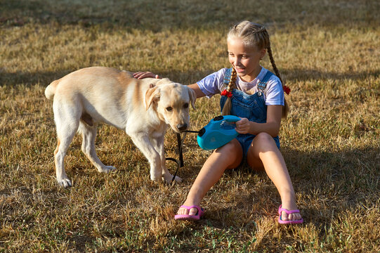 A little girl plays with a Labrador puppy on a walk