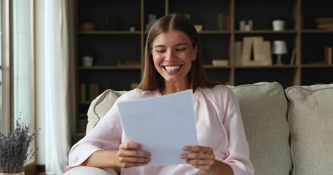 Overjoyed teenage female sit on sofa read paper letter about acceptance to college university celebrate great news of becoming student. Excited millennial businesswoman receive tax refund confirmation
