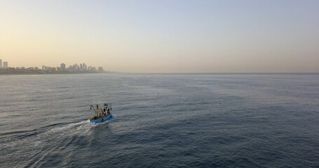 Small fishing boat sails off the coast of Tel Aviv, aerial
Drone view from Tel aviv Jafa at sunrise, 2021
 - obrazy, fototapety, plakaty