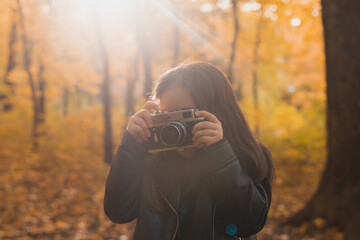 Child girl using an old-fashioned camera in autumn nature. Photographer, fall season and leisure concept.