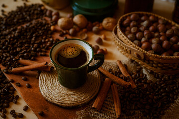 a cup of coffee on scattered coffee beans with cinnamon sticks and nuts