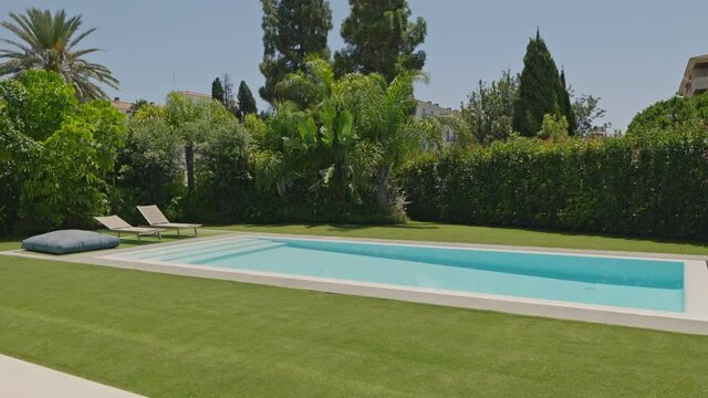 Swimming pool and empty sunbeds with trees and lawn.