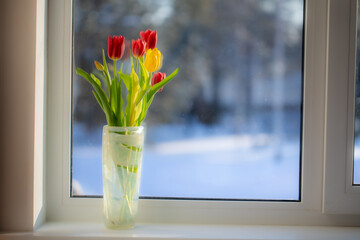 A bouquet of flowers is on the window. Outside the window, a sunny frosty snowy morning