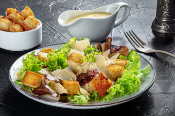 Chicken Caesar salad with the classic dressing, croutons, and pepper, on a black background