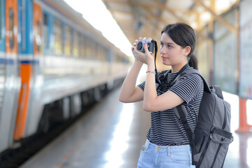 While waiting for a train, a young foreign female visitor carries a camera to take pictures.