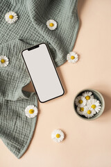 Flatlay of blank screen mobile phone, chamomile flower buds, aquamarine muslin cloth on neutral beige background. Aesthetic social media, blog template with mockup space. Flat lay, top view. - obrazy, fototapety, plakaty