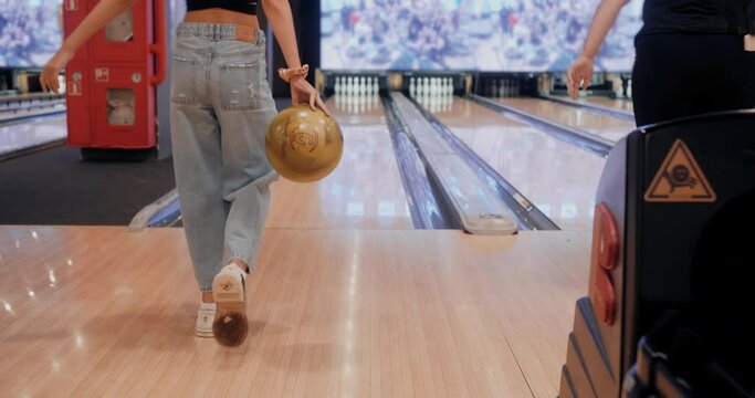 Teenage girl approaching and carrying ball in bowling. Happy teen girl rolling ball toward pins and lying on floor surface