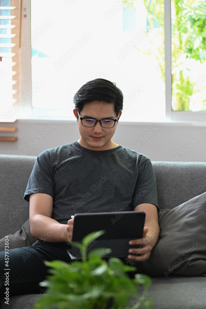 Poster handsome man sitting on sofa and browsing internet with computer tablet.