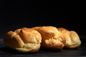 Profiteroles, puffs, popovers, eclaires on black background close up.