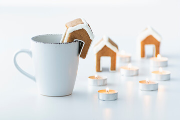 White mug with tea, small gingerbread house and candles. Christmas cozy holidays