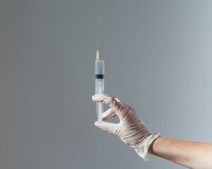 Syringe with needle and splashes from it in doctors hand in glove over gray background.