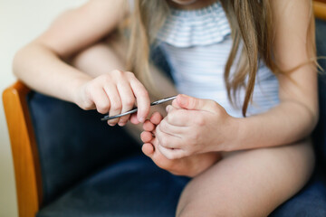 Kid girl cuts her toenails in bright real interior, lifestyle, hygiene and personal care, Child girl cuts her nails with scissors with copy space, top view. concept of children's independence