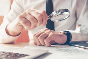 Cautious businessman reading contract agreement with magnifying glass
