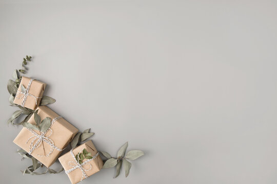 Composition of small gift boxes wrapped in craft paper with dried eucalyptus leaves on solid gray background. Modern minimal presents suitable for any occasion Neutral holiday backdrop with copy space