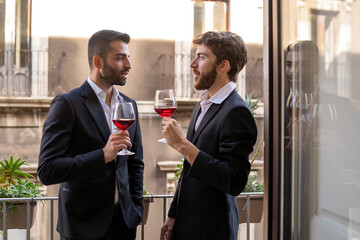 Businessmen in suite talking together against a window in an hotel room holding red wine glasses.