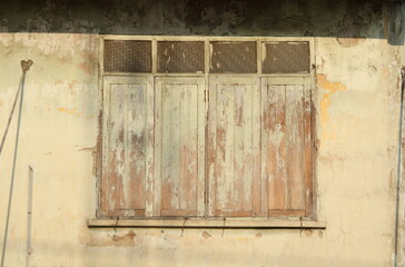 Painted wood window on light yellow painted wall of retro style building, color flake off surface of closed window and building.