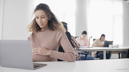 Happy female manager working on laptop, touching pregnant belly, motherhood