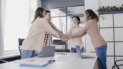 Happy sales managers joining hands in office, team building, work motivation