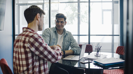 Young employees shaking hands working on advertising project in conference room