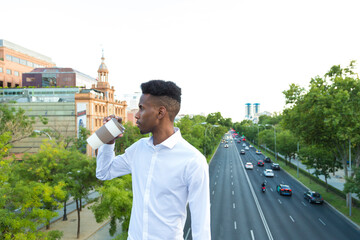 portrait young african american executive man drinking coffee in the street with traffic in the background