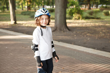 Charming boy wearing skating protective gear and helmet at the park, copy space