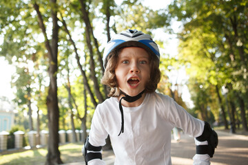 Excited young boy rollerblading at the park, wearing helmet