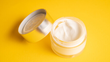 Open jar with white cream. Skincare. Moisturizer in the transparent container on yellow