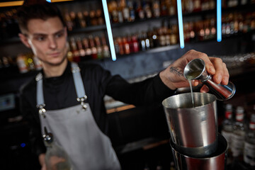Bartender in apron adds ingredient to shaker