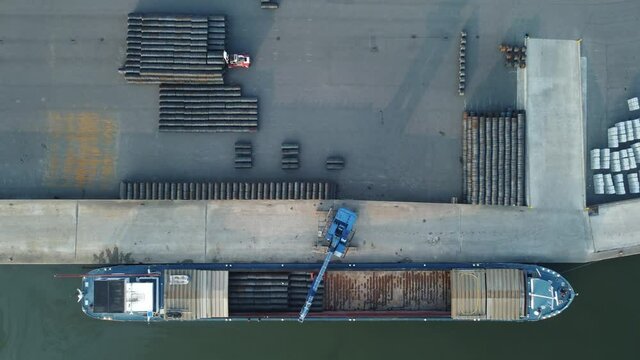 Aerial top down shot of crane loading barge and fork lift moving goods while the drone camera is zooms out