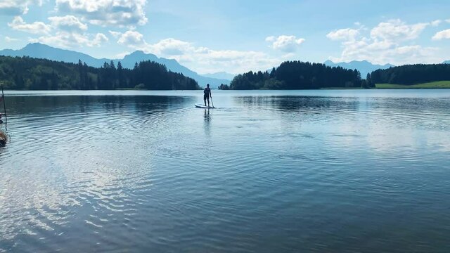 Trend Watersport SUP Standup paddling of a sportive man in summer on a lake with clouds and mountains in the background on a sunny day, Forggensee, Allg&auml;u Bavaria, Alps