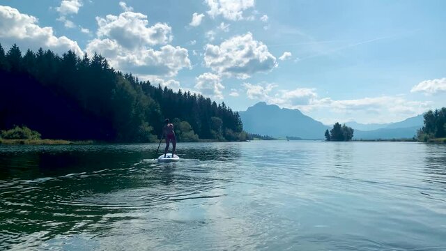 Trend Watersport SUP Standup paddling of a sportive man in summer on a lake with clouds and mountains in the background on a sunny day, Forggensee, Allgäu Bavaria, Alps